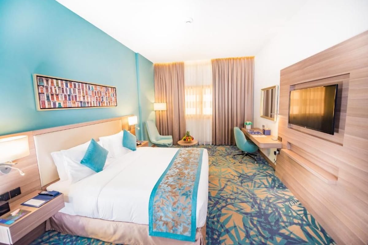 Una habitación de hotel con una cama grande, un escritorio, un televisor y una obra de arte colgada en la pared.