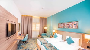 Een hotelkamer met twee bedden, een bureau, een televisie en een groot raam met gordijnen.