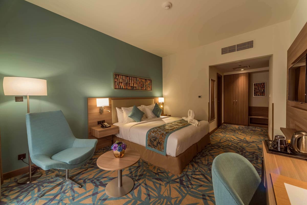Een hotelkamer met een bed, een bureau, een stoel, een lamp en een decoratief object aan de muur.
