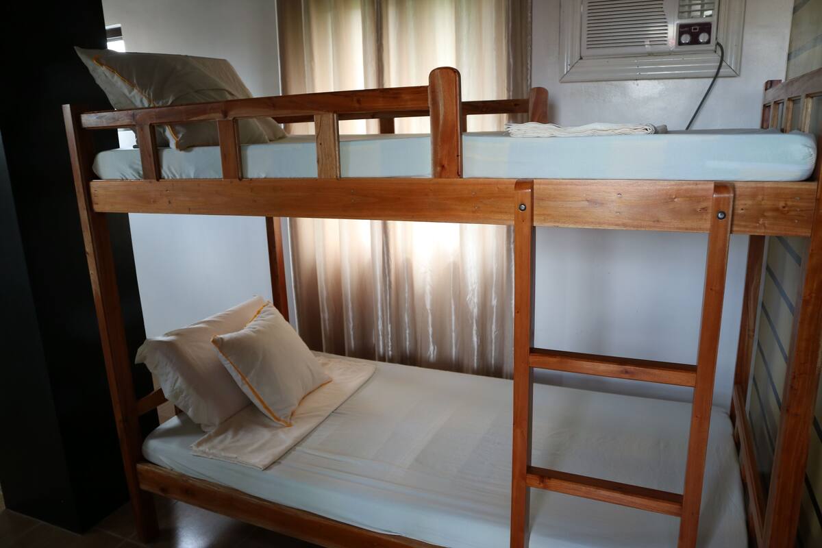 A bunk bed with a mattress and pillows, a window with curtains, and a wall-mounted air conditioning unit.