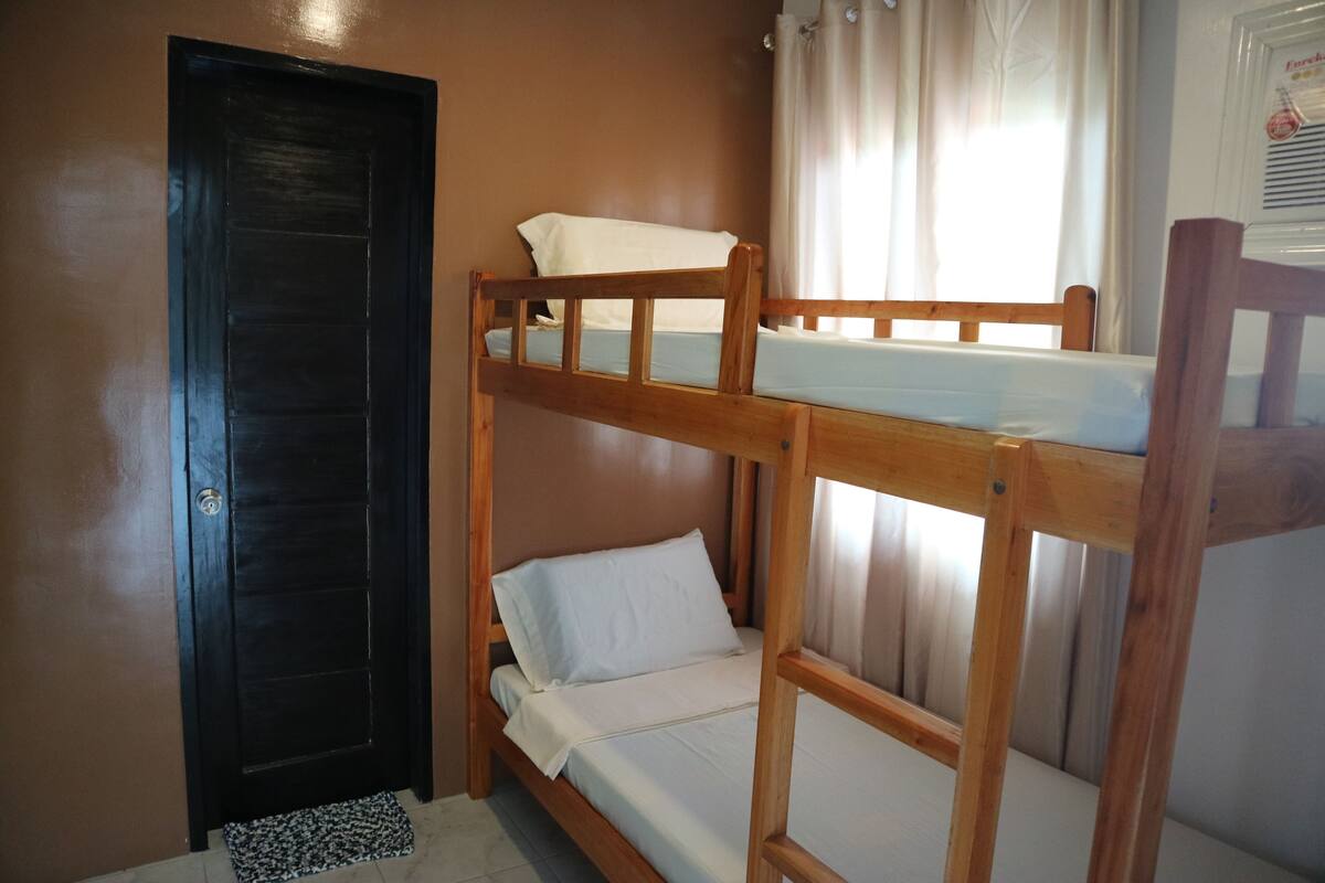 A bunk bed room with a door and a window with curtains.