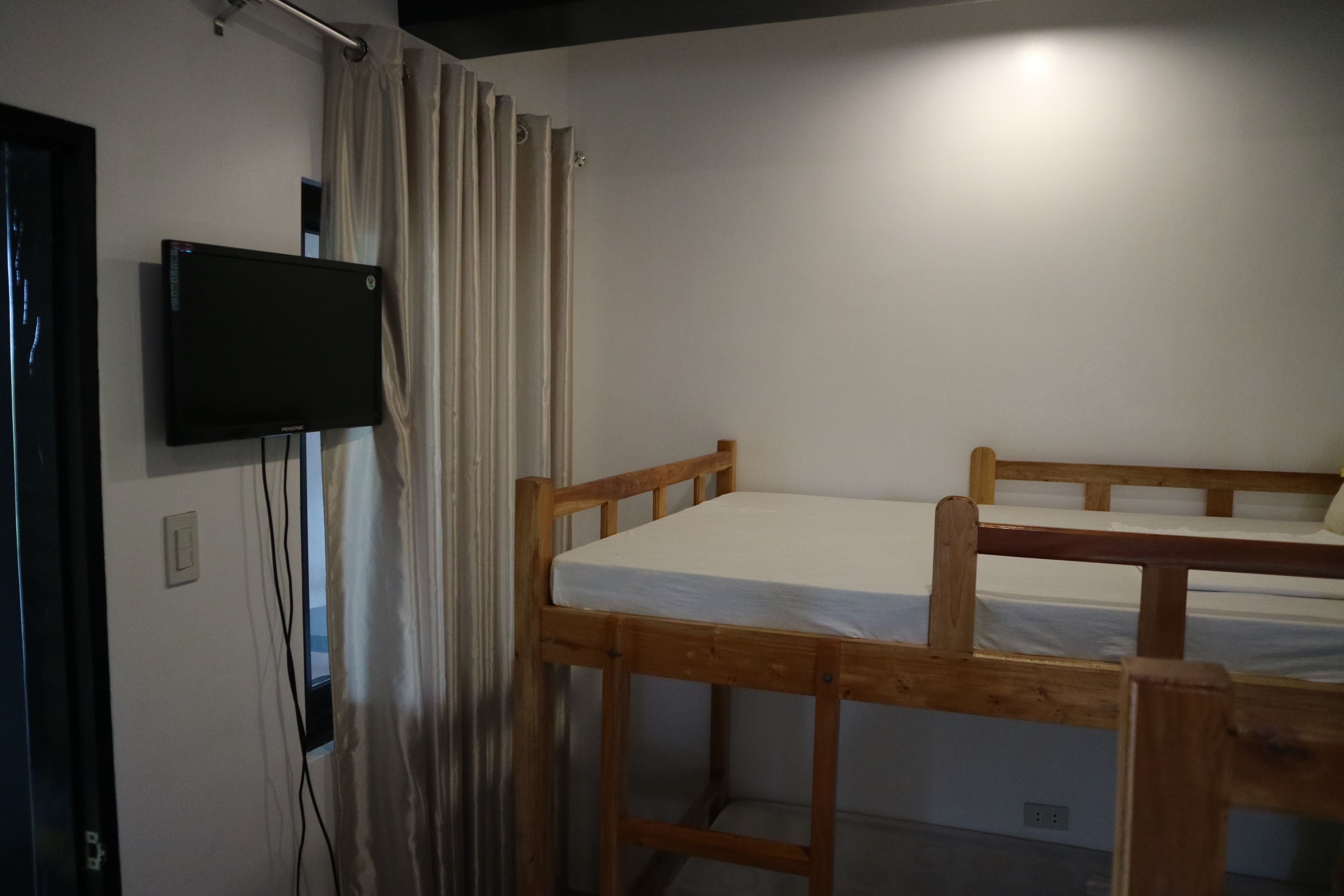 Une chambre avec un lit superposé en bois, un téléviseur fixé au mur et un rideau.