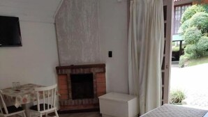 A bedroom with a bed, a small table with chairs, a fireplace, and a view of the outdoors.