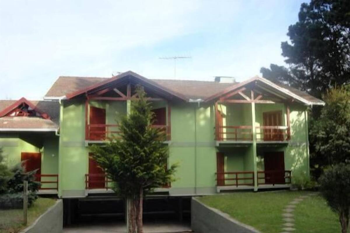 A two-story residential building with a green facade, red window frames, and a small balcony on the upper floor.