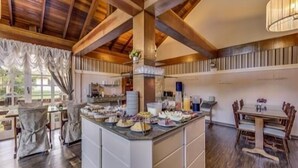 A breakfast bar with various food items, a dining area with wooden chairs, and a high ceiling with exposed beams.