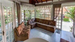 A spacious living area with a large L-shaped sofa, a small round table, and a view of a garden through large windows.