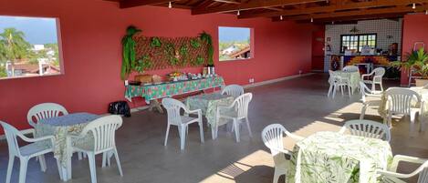 A spacious indoor area with high ceilings and a red wall. There are multiple tables and chairs arranged for dining.