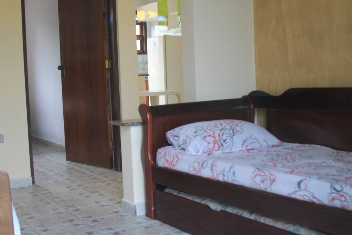 Ein Schlafzimmer mit einem hölzernen Bett, einer weißen Wand und einem Fliesenboden.