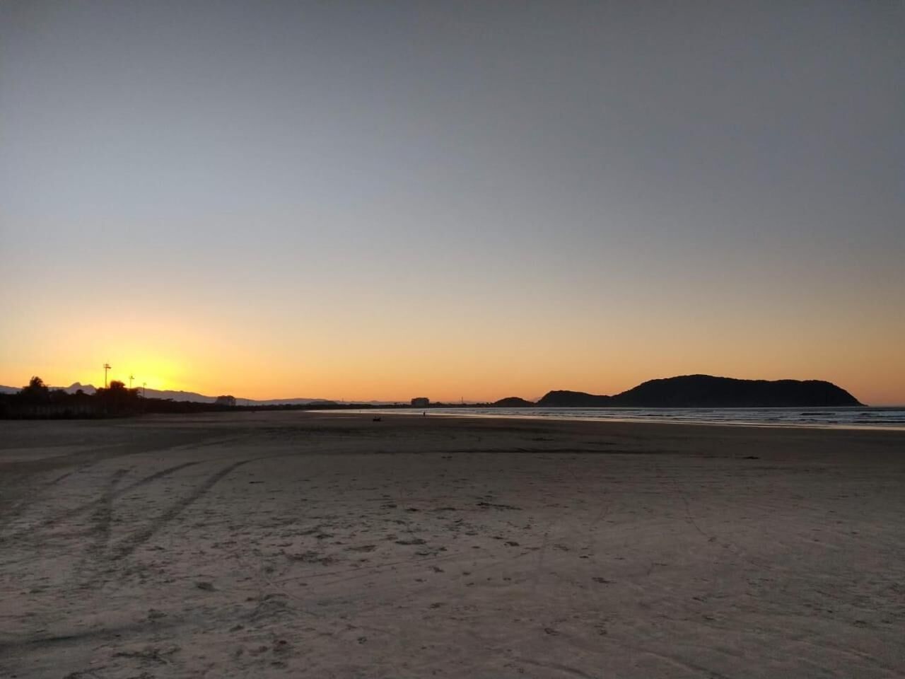 Una playa con atardecer, colinas lejanas y cielo despejado.