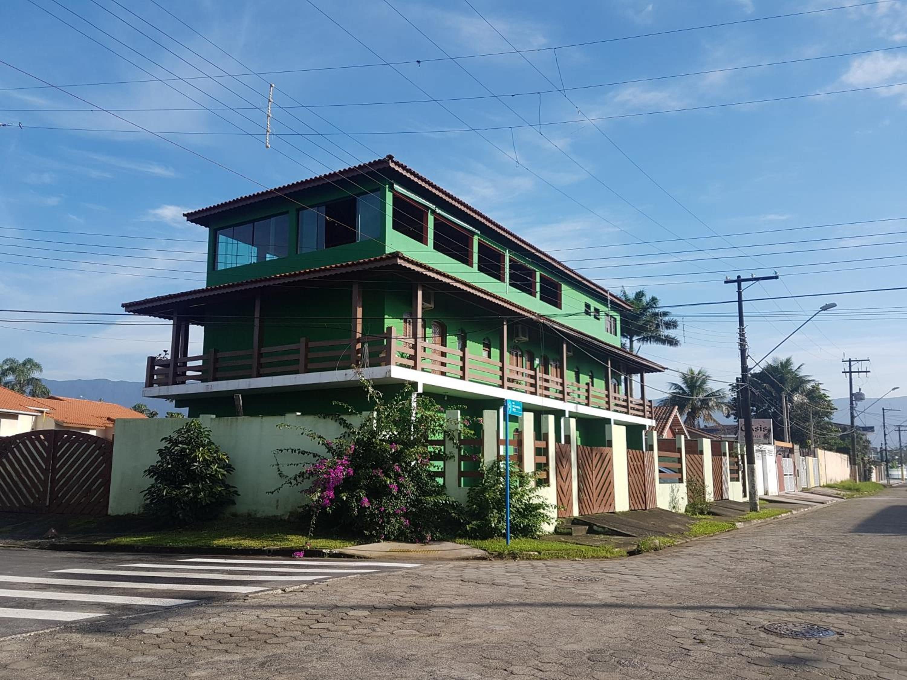 Un edificio de dos pisos con un balcón, rodeado de follaje y un cielo despejado.