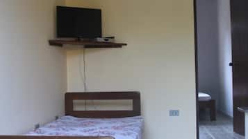 Ein kleiner, einfacher Raum mit einem Bett, einem an der Wand befestigten Fernseher und einer Tür zu einem weiteren Raum.