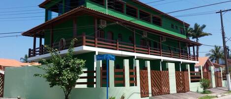 Un edificio de dos pisos con fachada verde, balcones de madera y un cartel que indica uso comercial o de oficinas.