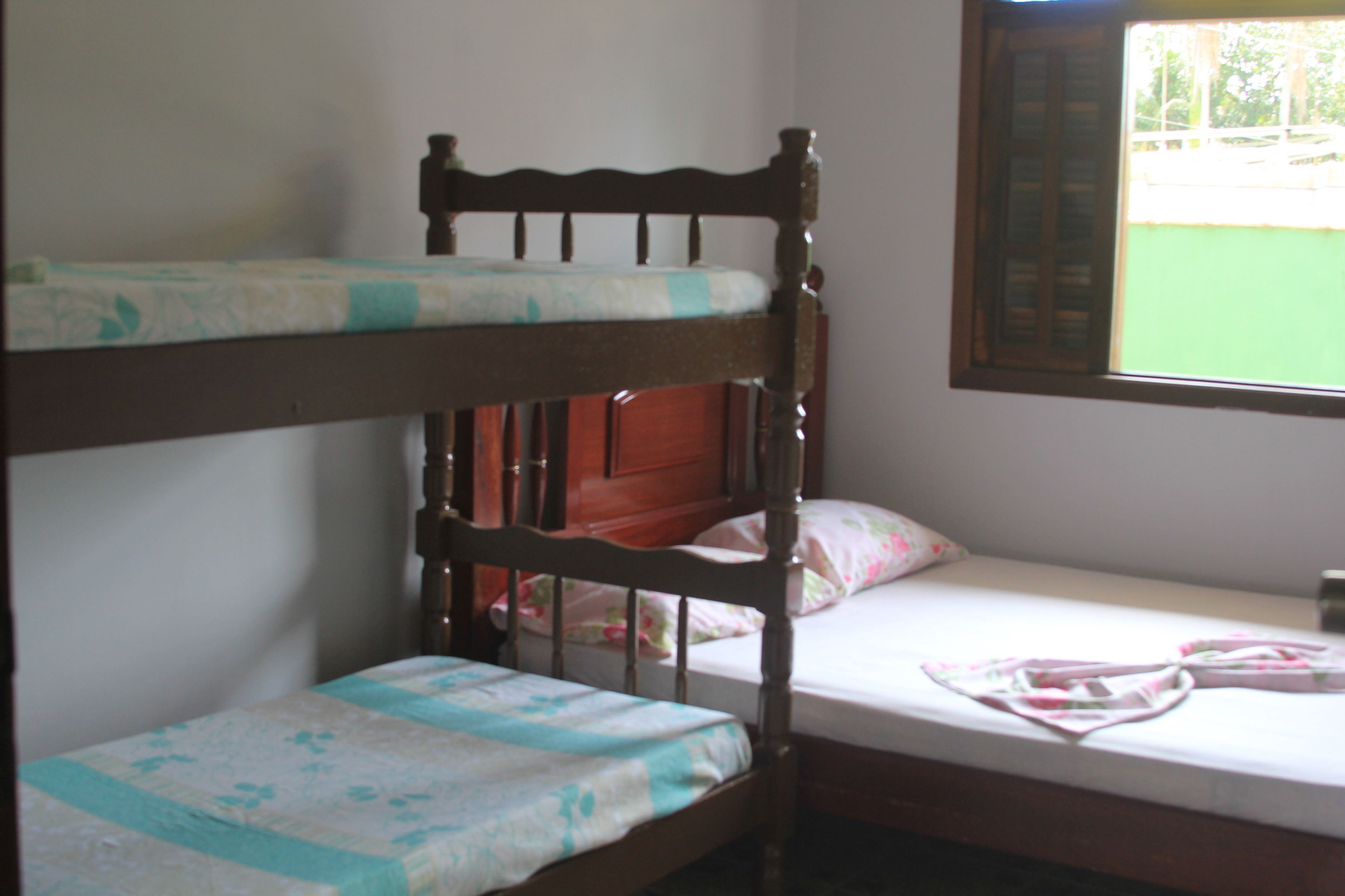 A bunk bed with a wooden headboard, a lower bunk with a floral bedspread, and a single bed with a pink floral bedspread.