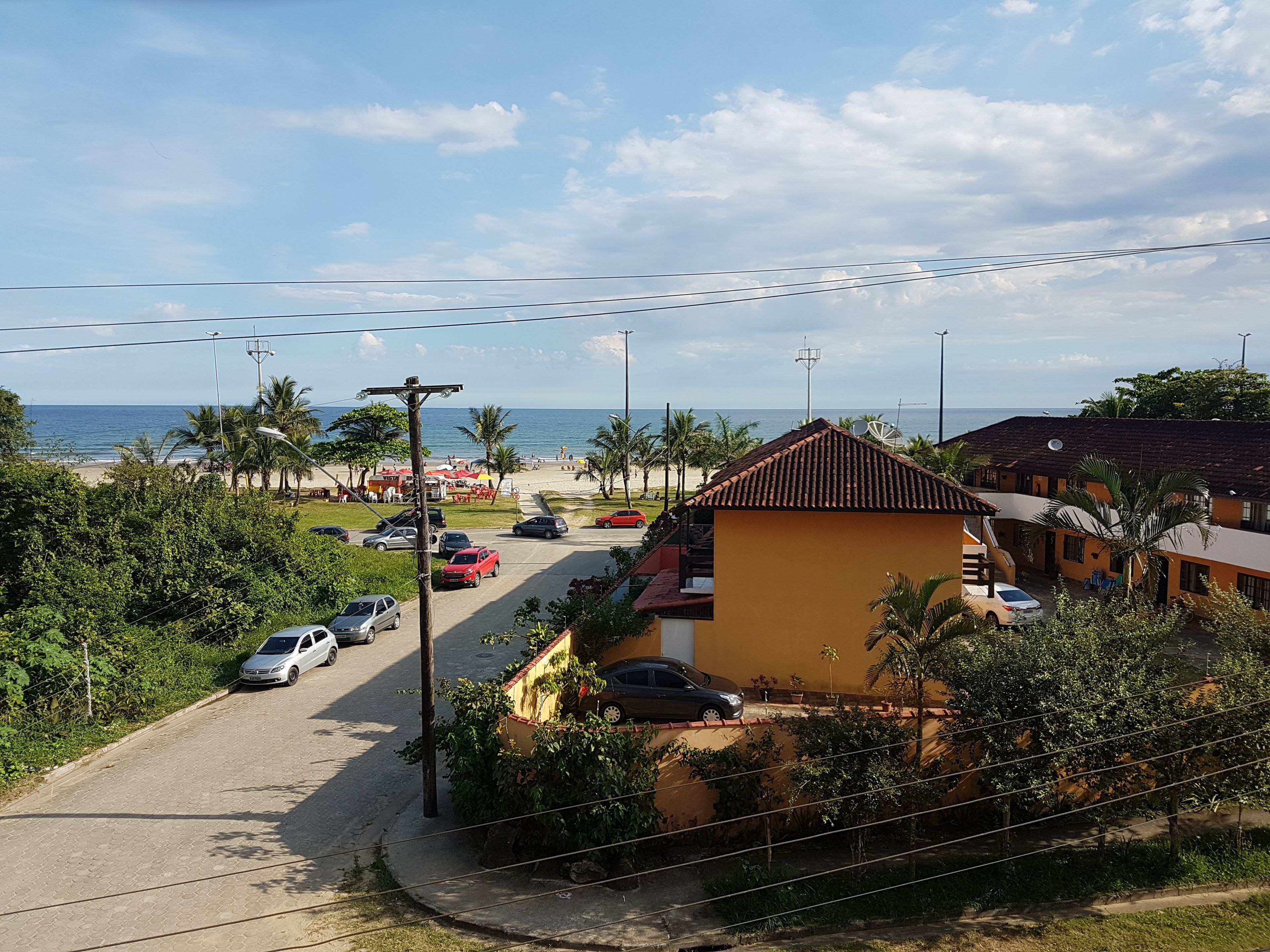 A coastal residential area with a paved road, parked cars, and a beach in the background.