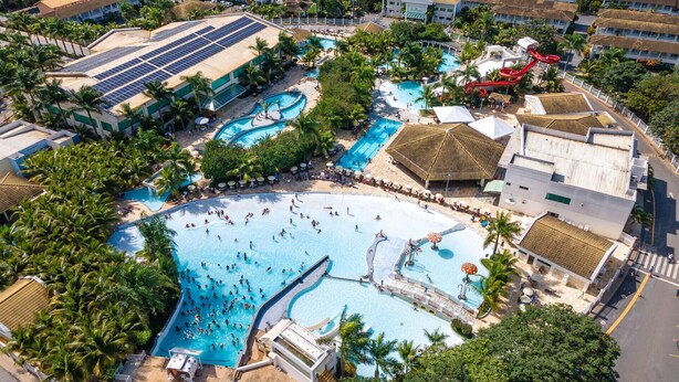 An aerial view of a resort with multiple swimming pools, palm trees, and a red water slide. - Diroma Lacqua I - Direto com o Grupo Diroma - Acesso ao Acqua Park com Café da Manhã (Caldas Novas)