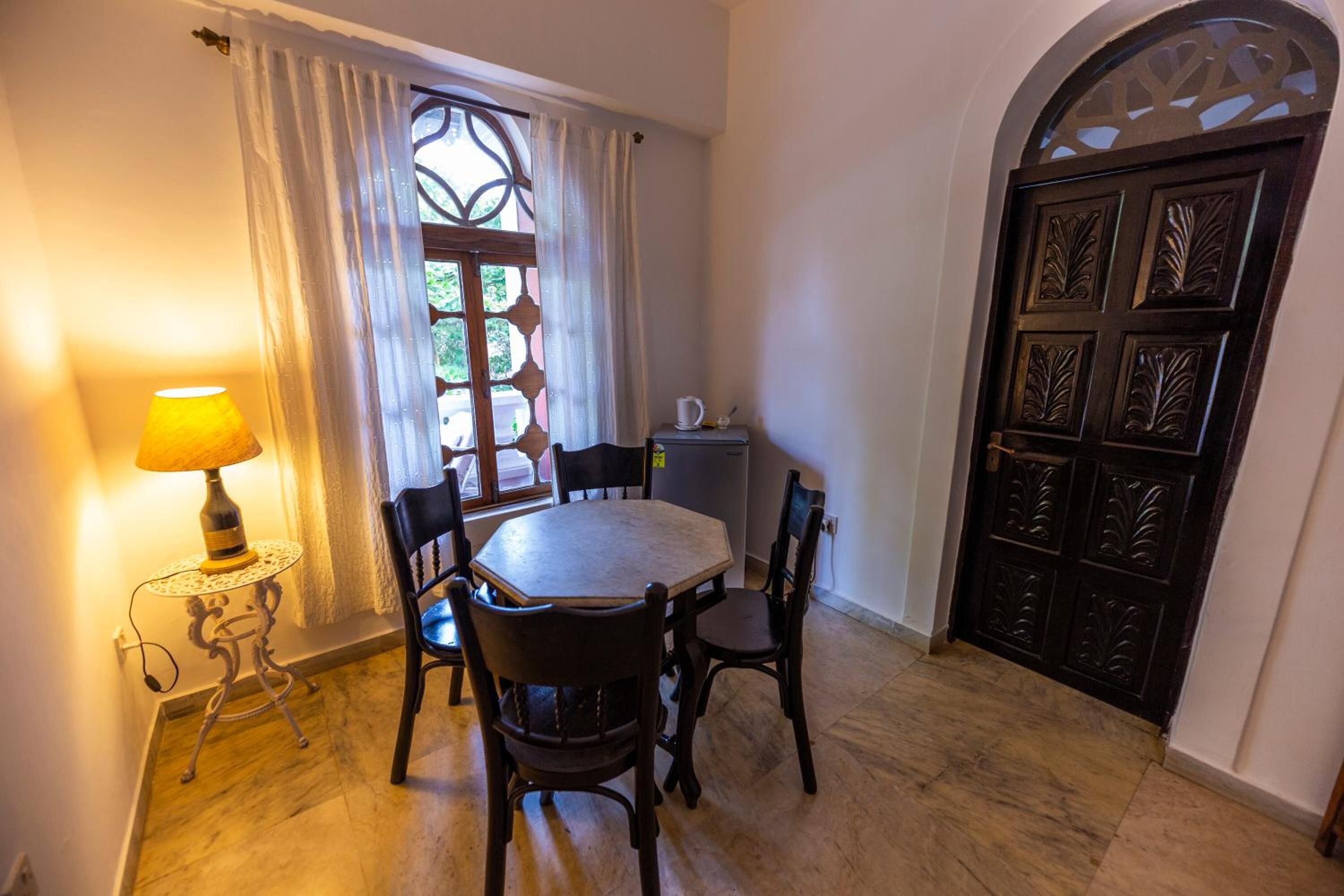A dining area with a round table, four chairs, a lamp, and a window with curtains.