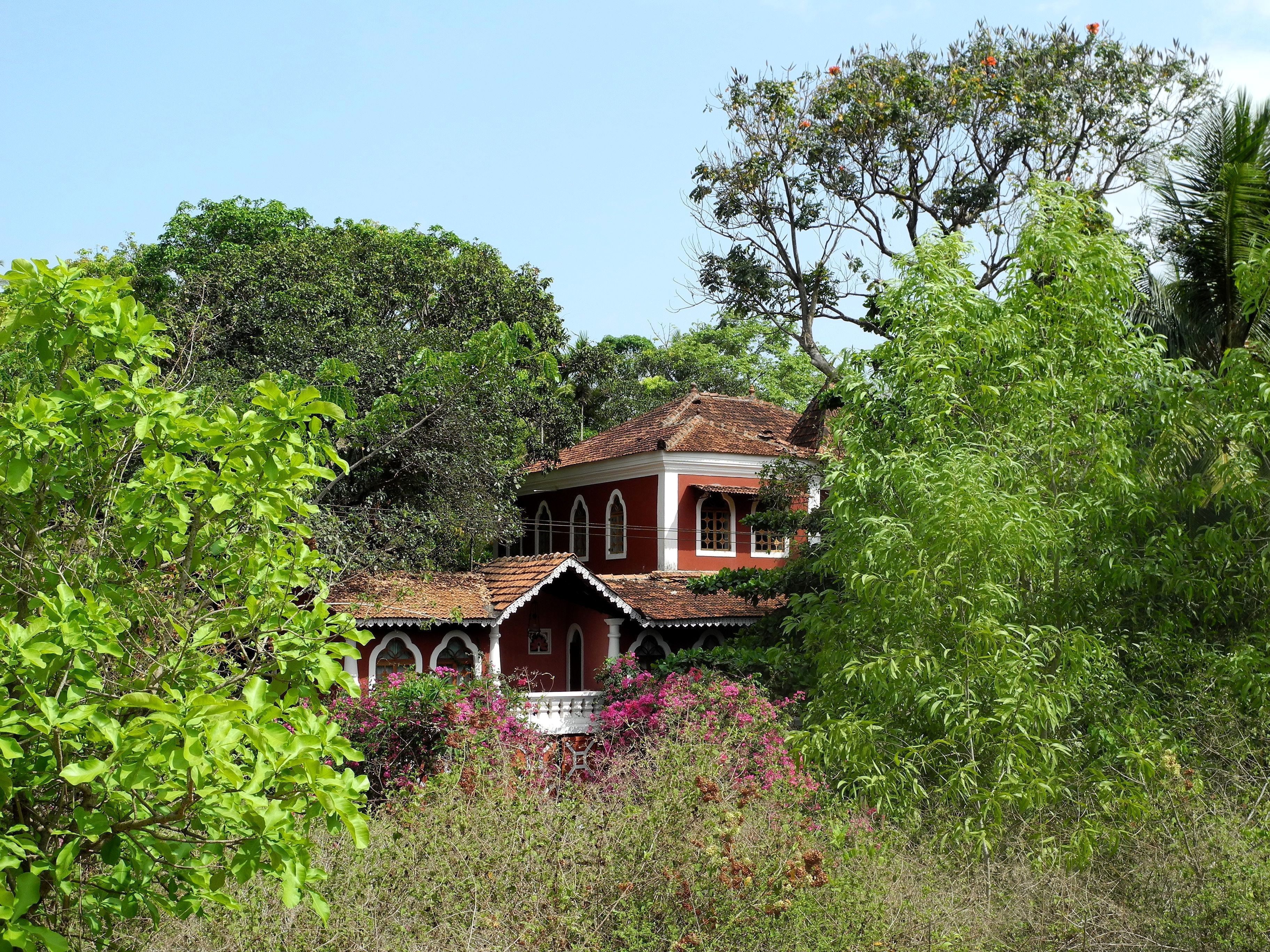 A traditional house with a red roof and white walls, surrounded by lush greenery and trees.
