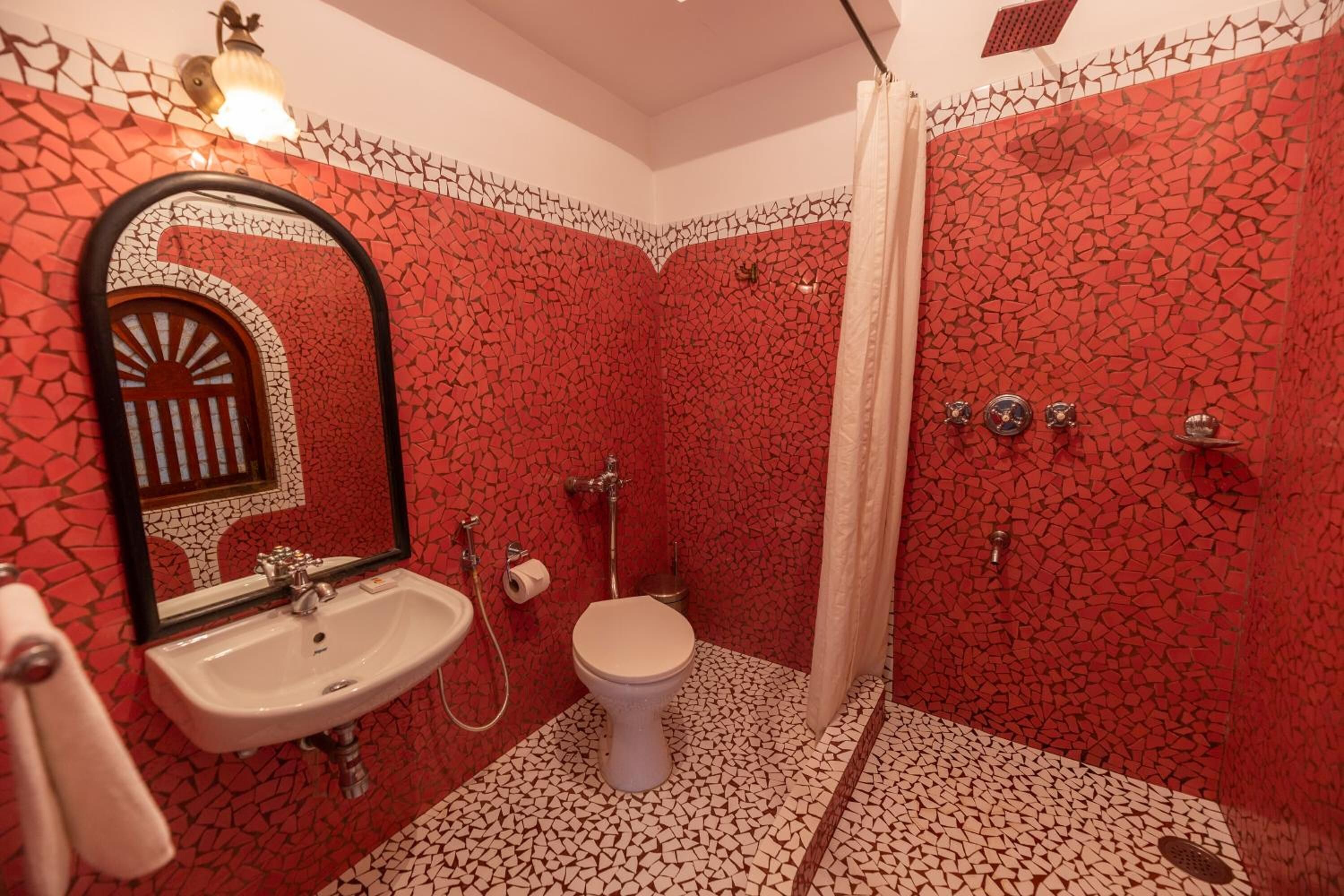 Un baño con pared de mosaico rojo, un lavamanos blanco, un inodoro y una zona de ducha.