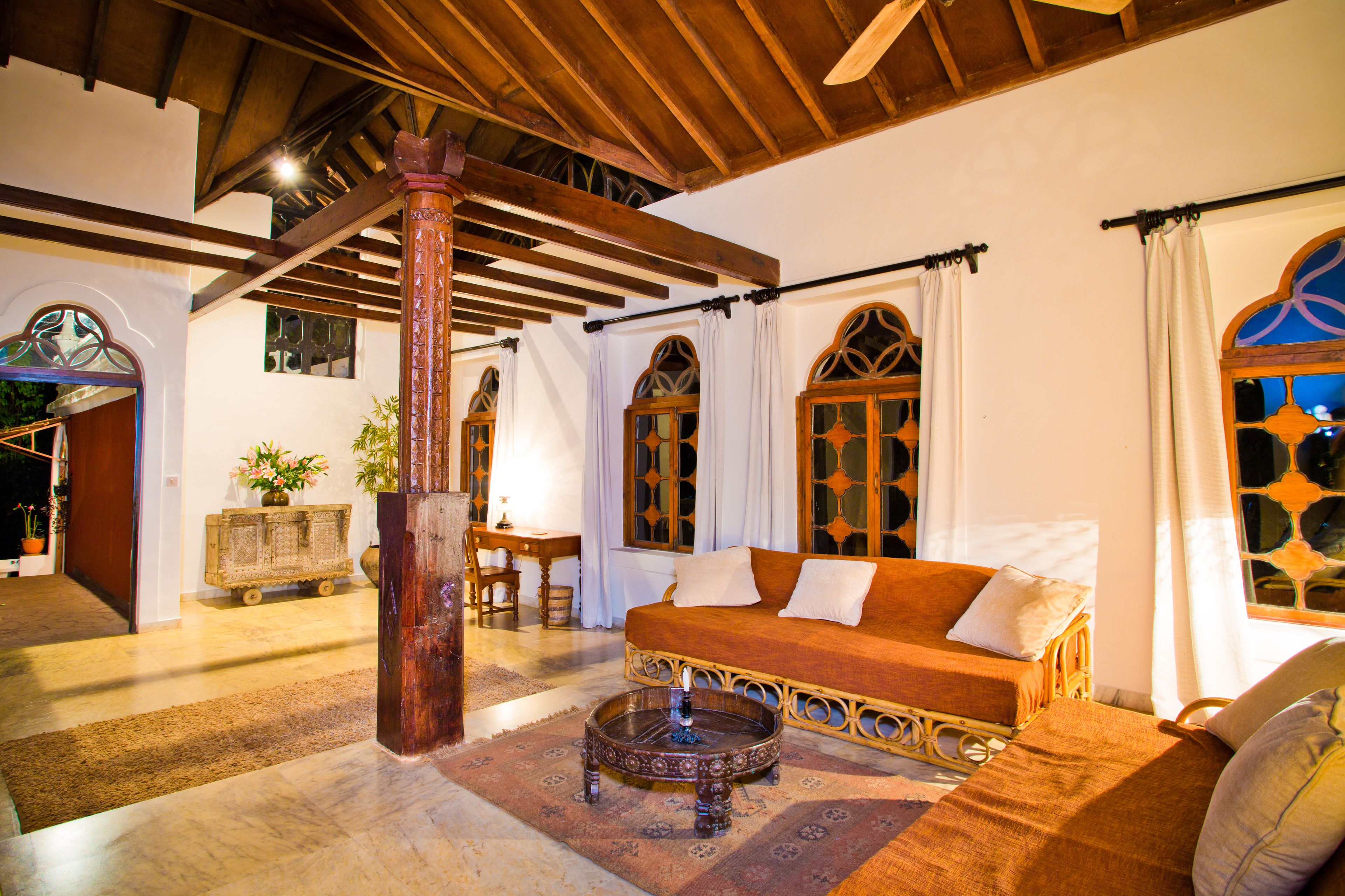 Una habitación acogedora con techo de madera, un sofá con cojines, una mesita de centro redonda y una ventana con cortinas.