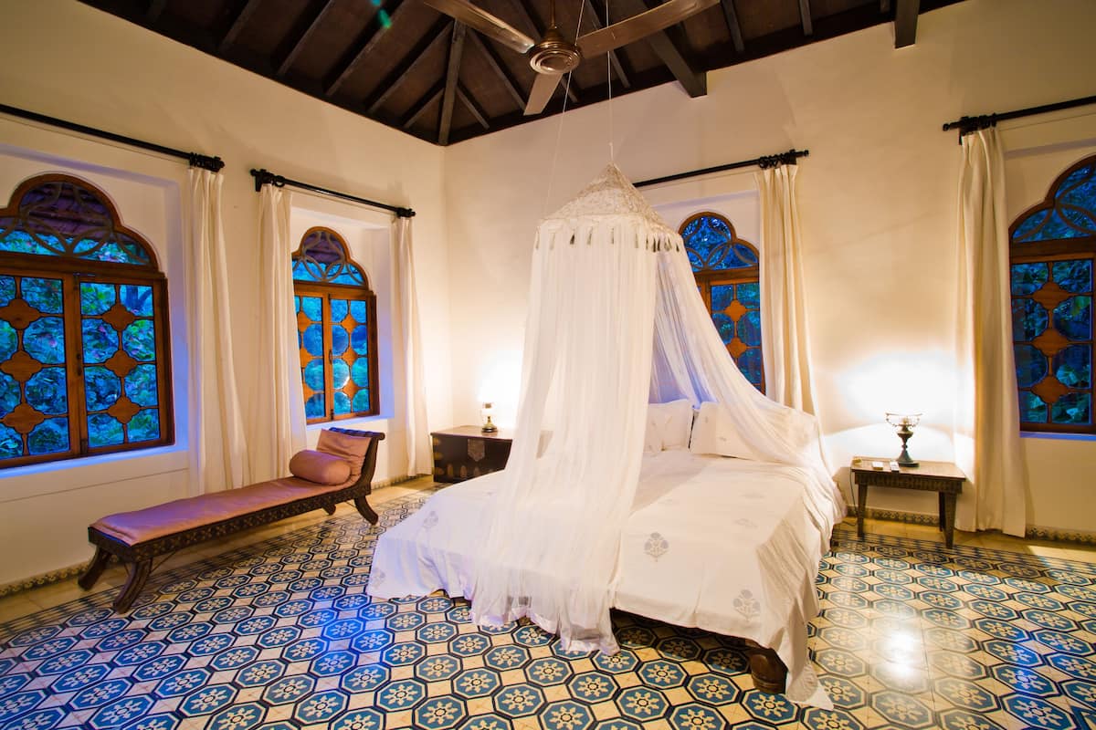 A bedroom with a four-poster bed, a bench, and a nightstand.