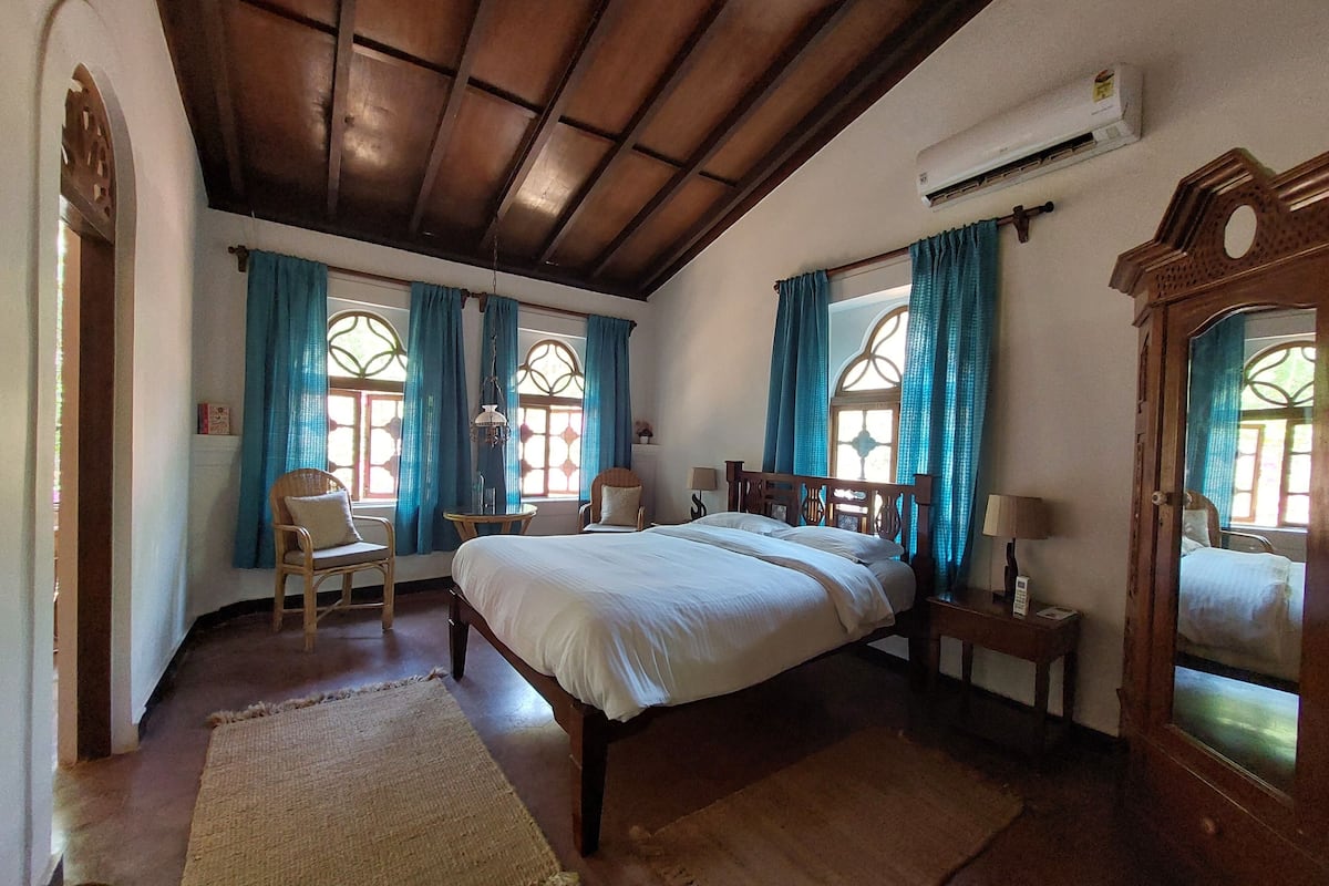 A bedroom with a large bed, two chairs, a small table, and a mirror.