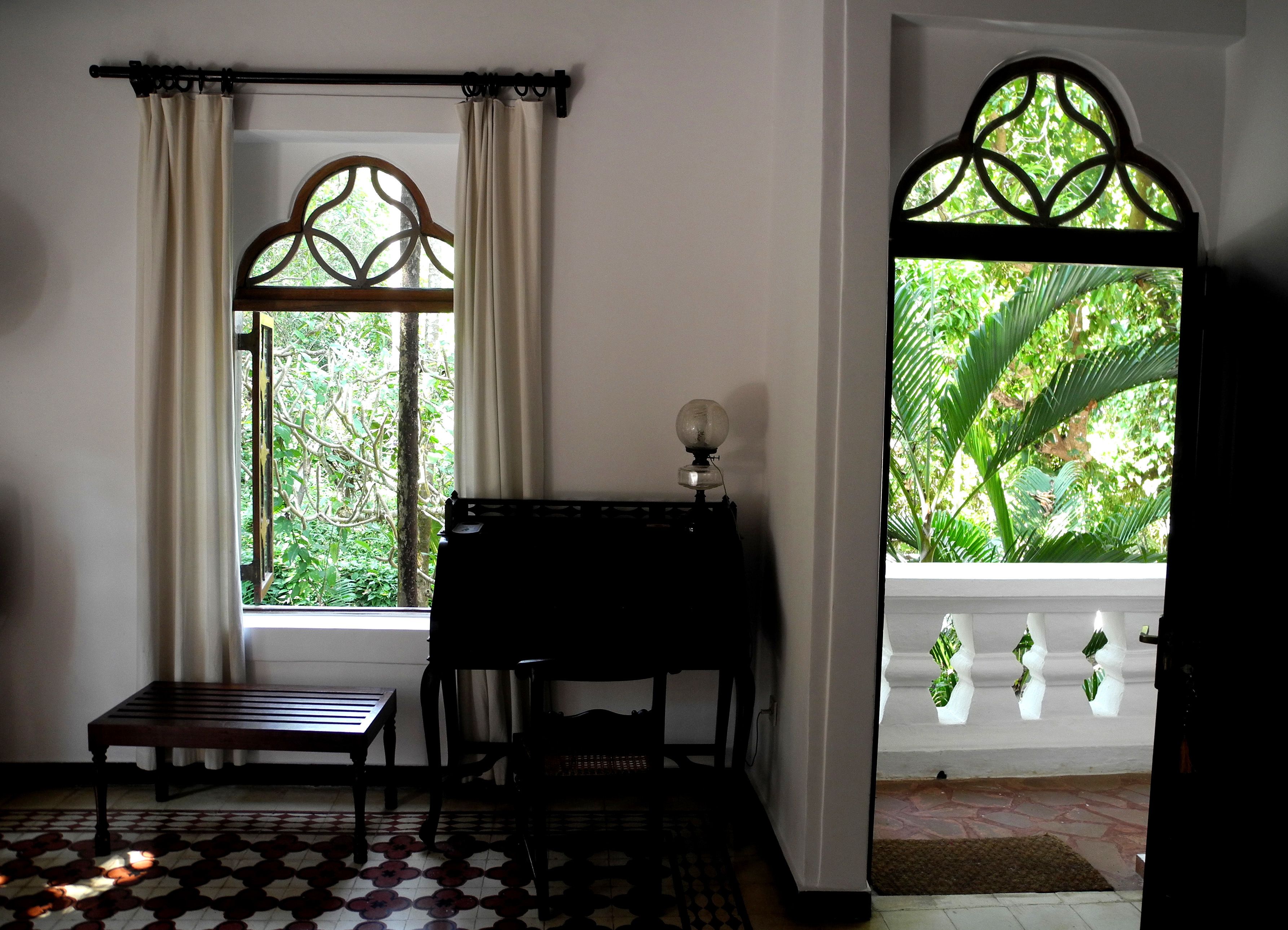 A room with a wooden bench, a small table, and a globe. There is a window with curtains and a view of greenery outside.