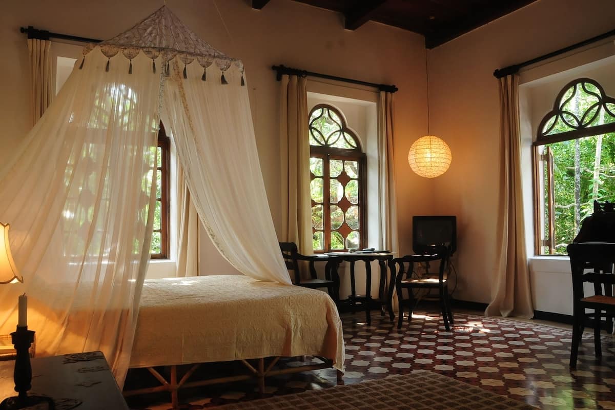 A bedroom with a canopy bed, a checkered floor, and a television on a wooden table.