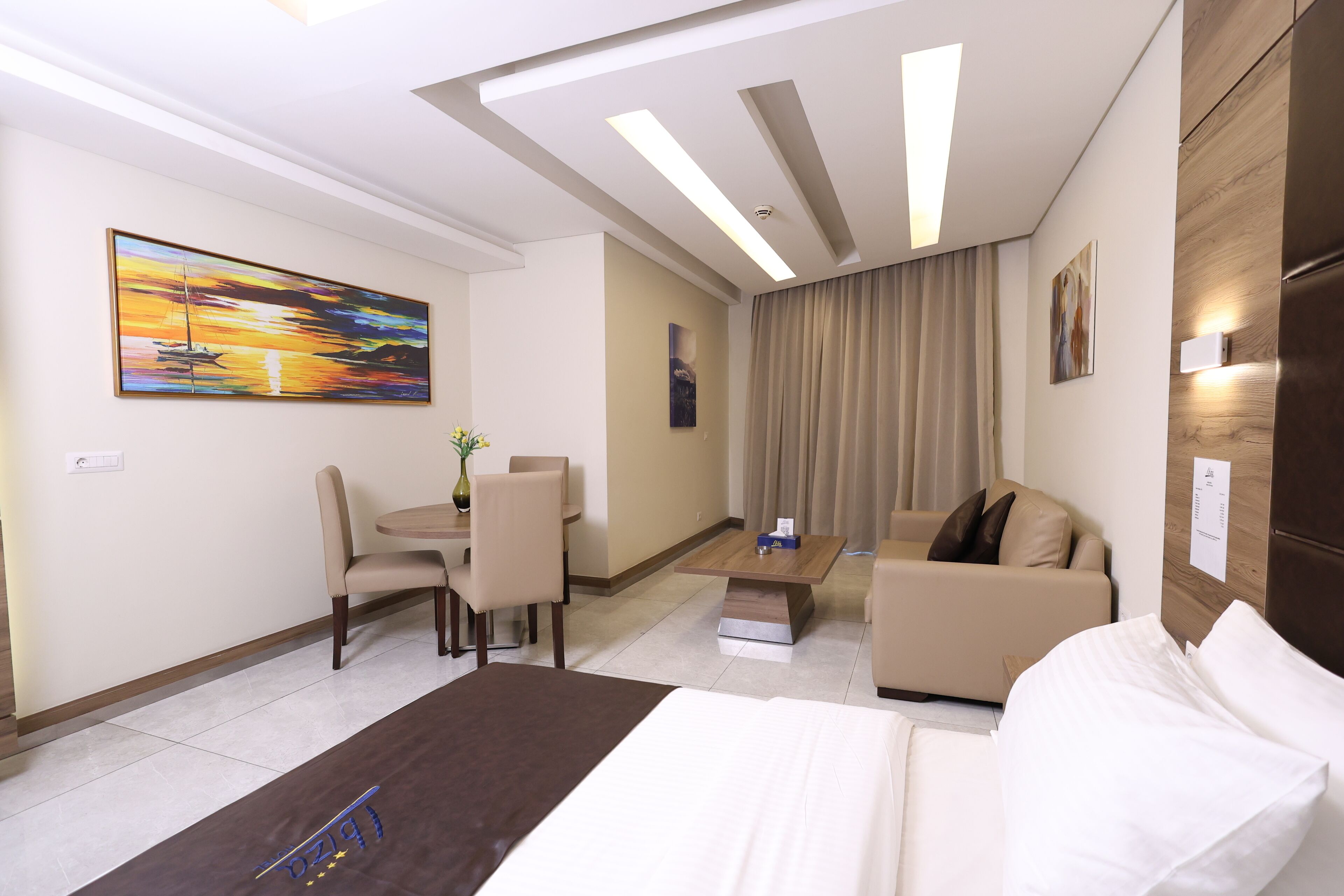 Habitació d'hotel amb un llit, un sofà, una taula de treball i cadires, i un quadre a la paret.