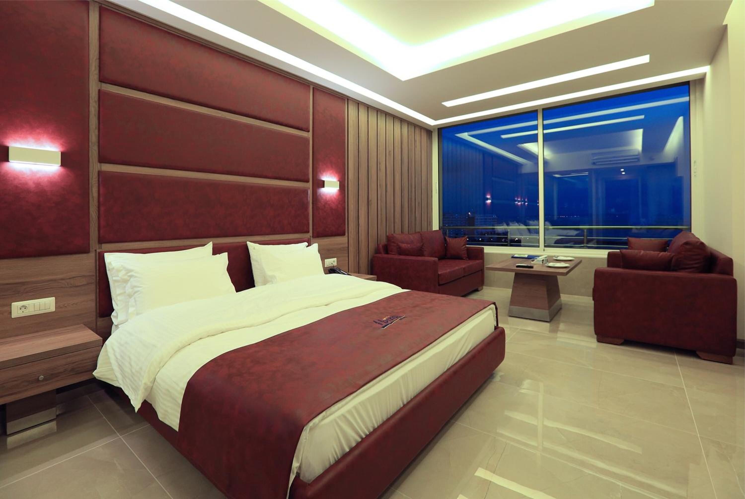 Una moderna camera d'hotel con un letto grande, un'area salotto con divani, un tavolino da caffè e un'ampia finestra con vista sulla città.