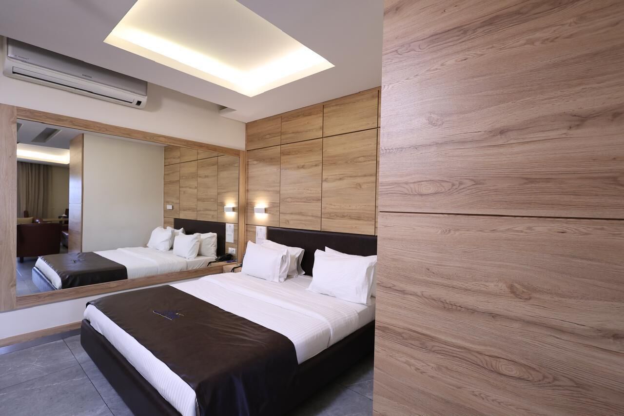 A modern hotel room with a large bed, a wooden headboard, a mirror, and a ceiling air conditioner.