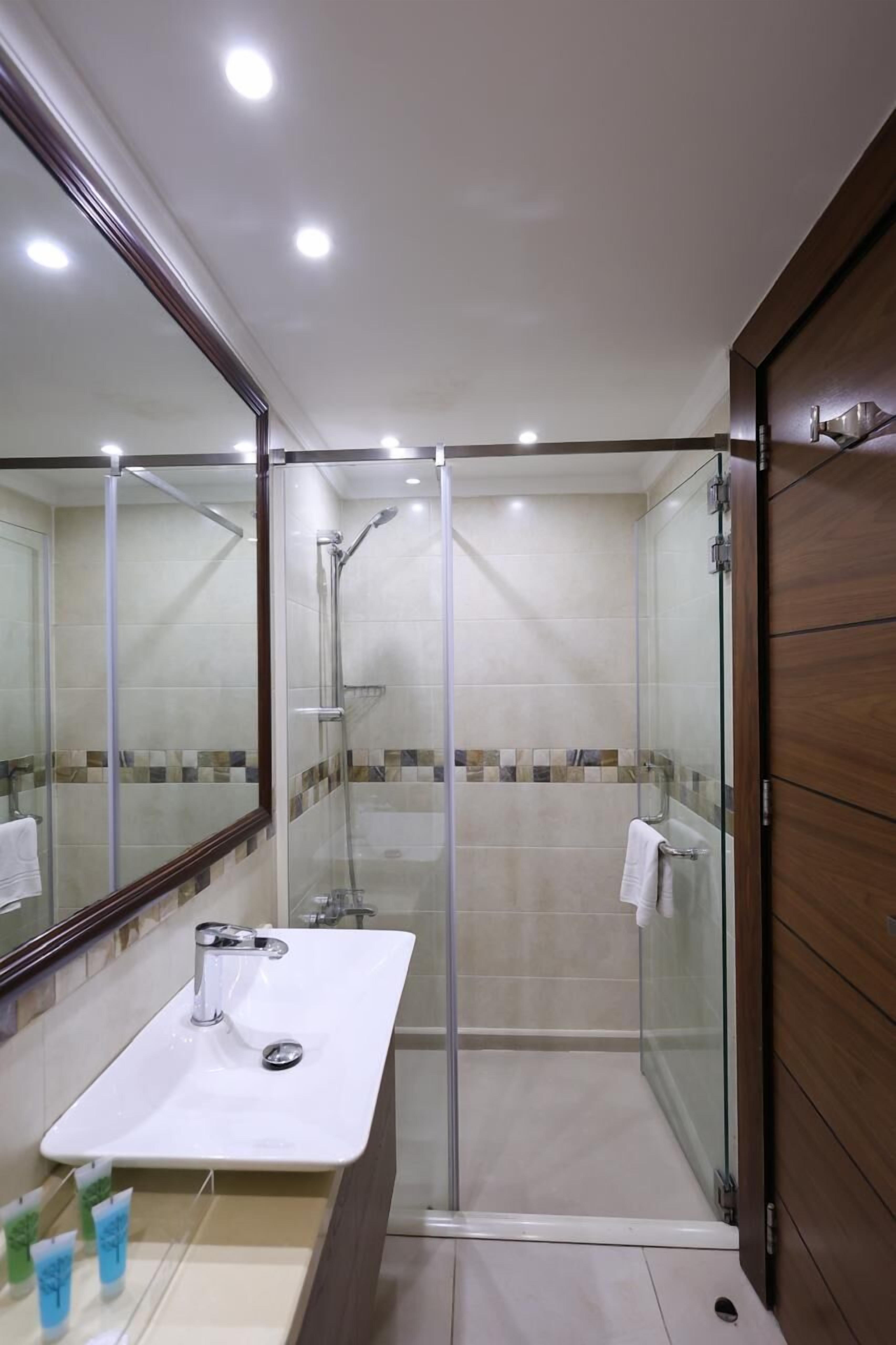 A modern bathroom with a glass-enclosed shower, a white sink, and a large mirror.