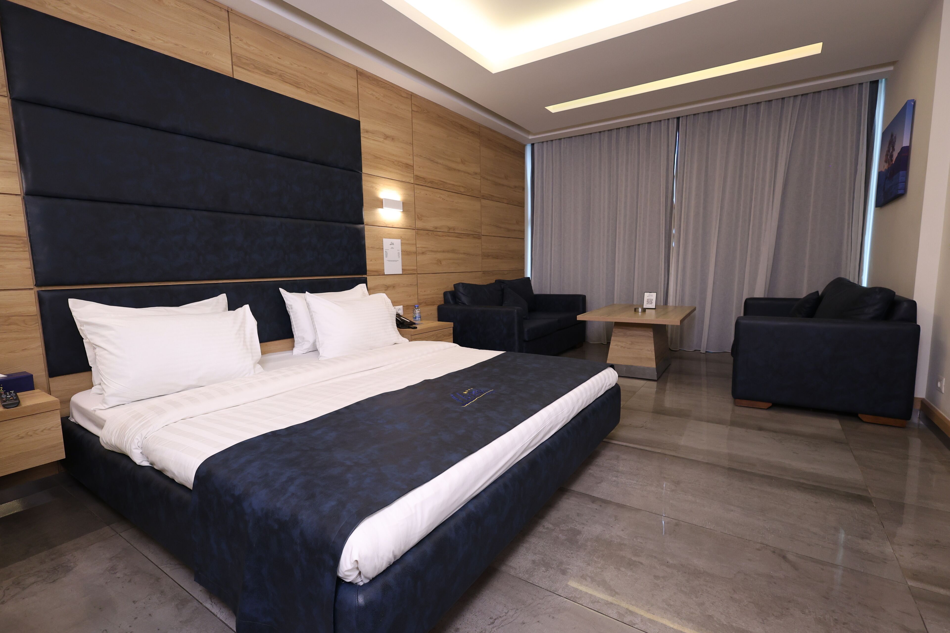 Une chambre d’hôtel moderne avec un grand lit, deux canapés, une petite table et une grande fenêtre avec des rideaux.