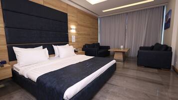 Une chambre d’hôtel moderne avec un grand lit, deux canapés, une petite table et une grande fenêtre avec des rideaux.