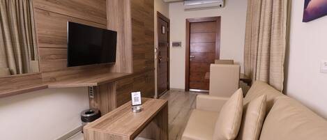 Una sala de estar moderna con un televisor de pantalla plana, paneles de madera, un sofá color beige y una mesita.