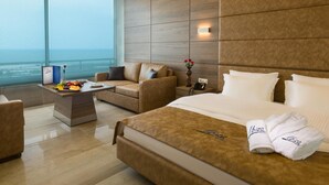 A modern hotel room with a large bed, a sofa, a desk with a laptop, and a view of the ocean.