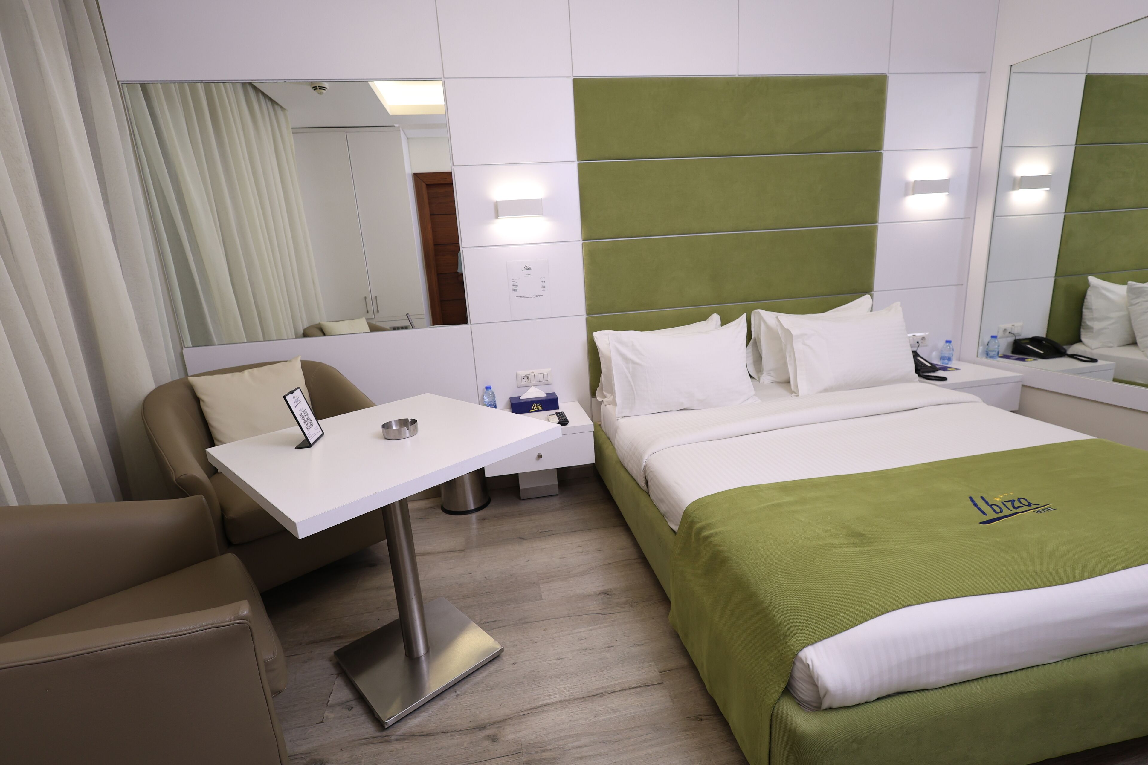 A hotel room with a bed, a desk, a chair, a mirror, and a nightstand.