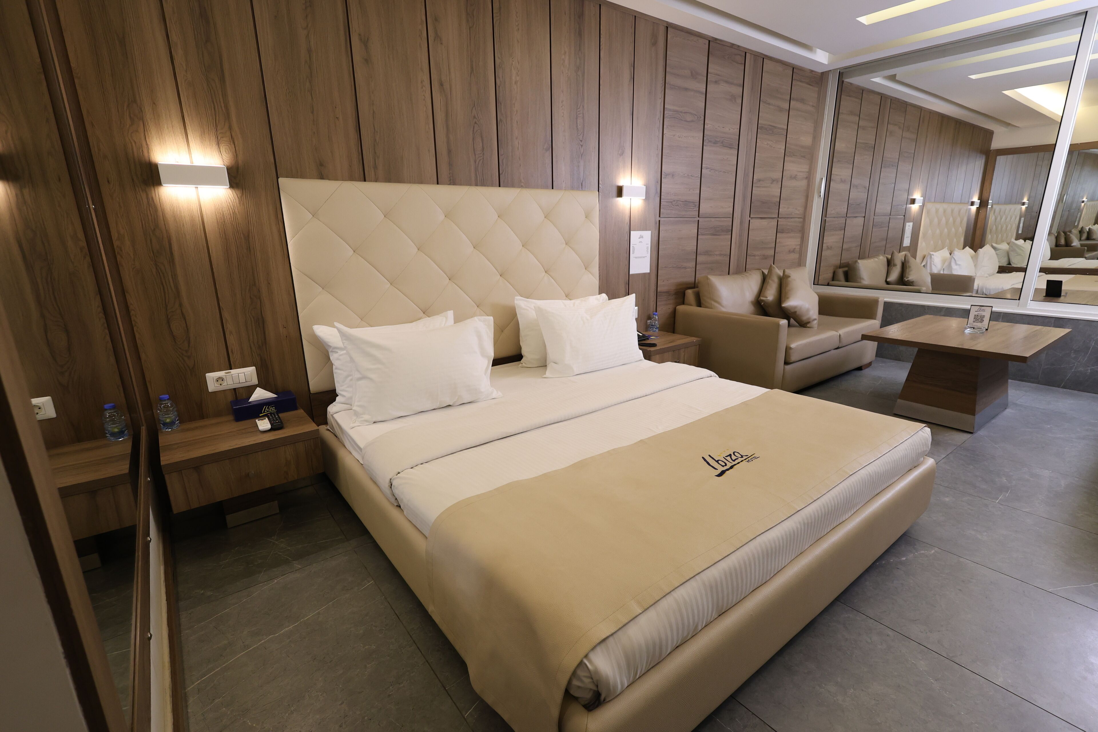 Habitación de hotel moderna con una cama grande, un sofá, una mesita y un espejo.