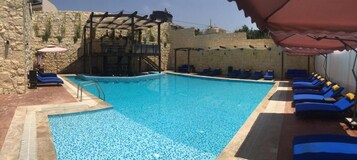 Una piscina al aire libre, sombrillas, sillones reclinables de piscina