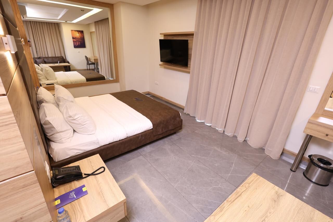 Habitación de hotel con cama, escritorio, silla, televisor y cubo de basura.