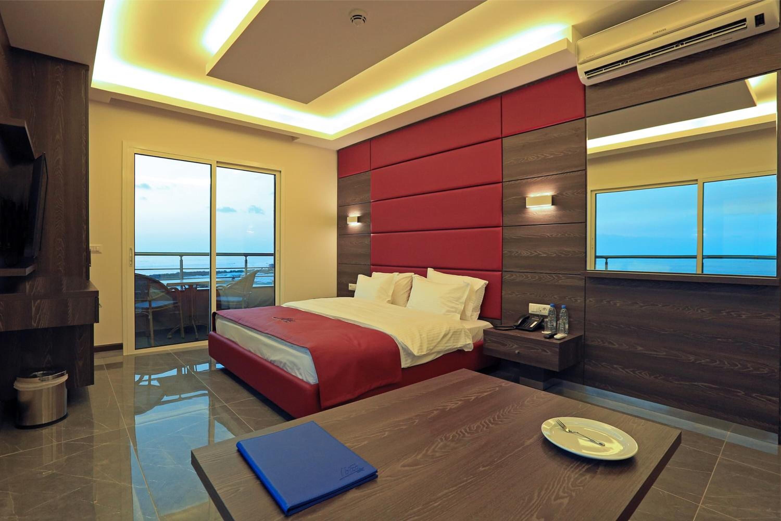 A modern hotel room with a large bed, a desk, a chair, and a view of the sea.