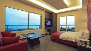 A modern hotel room with a balcony, a TV, a bed, a sofa, and a dining table.