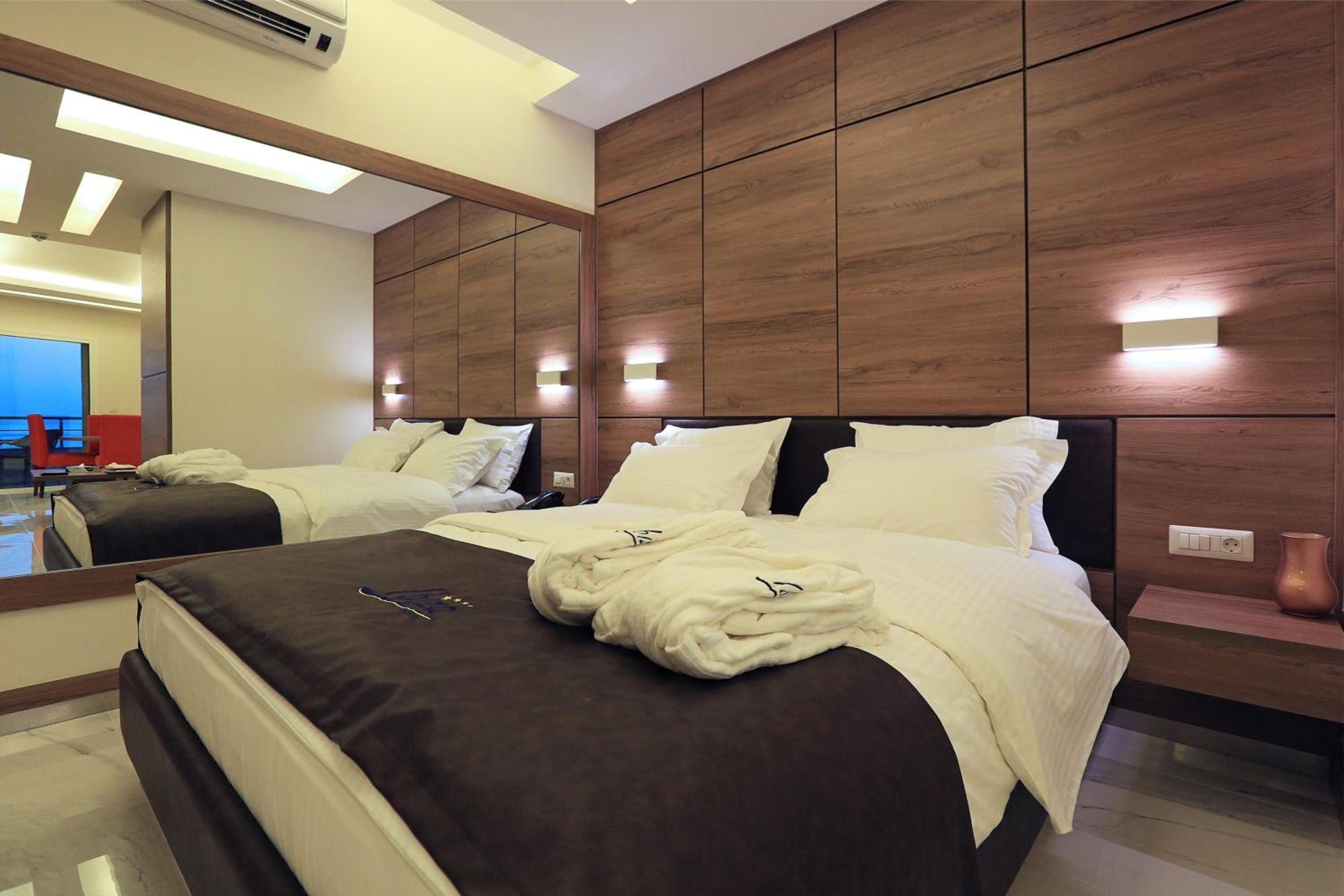 Une chambre d’hôtel moderne avec deux lits, un grand miroir et un mur recouvert de panneaux en bois.