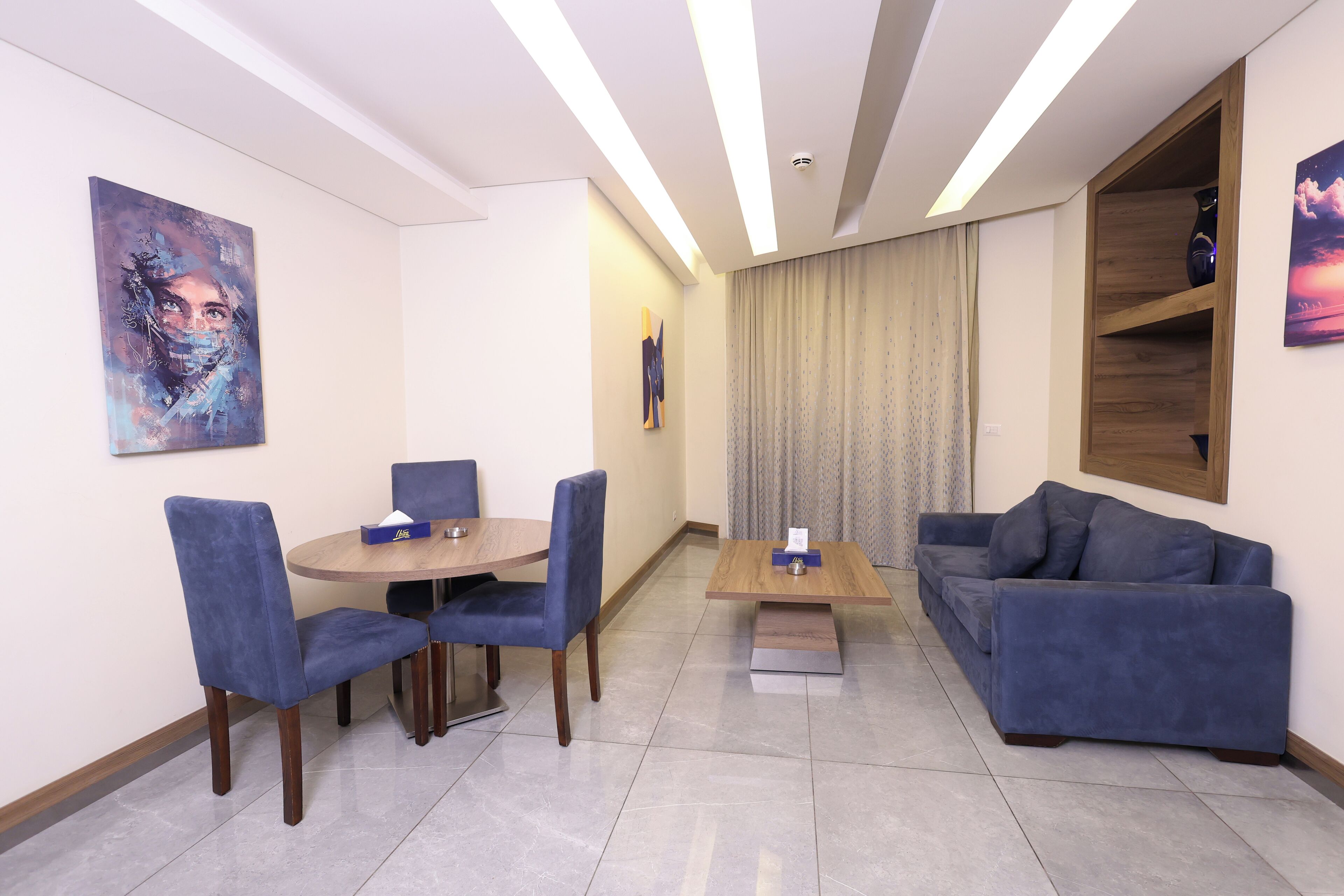 Un salón moderno con una mesa de comedor redonda, sillas tapizadas en azul, un sofá azul y una mesa de centro de madera.