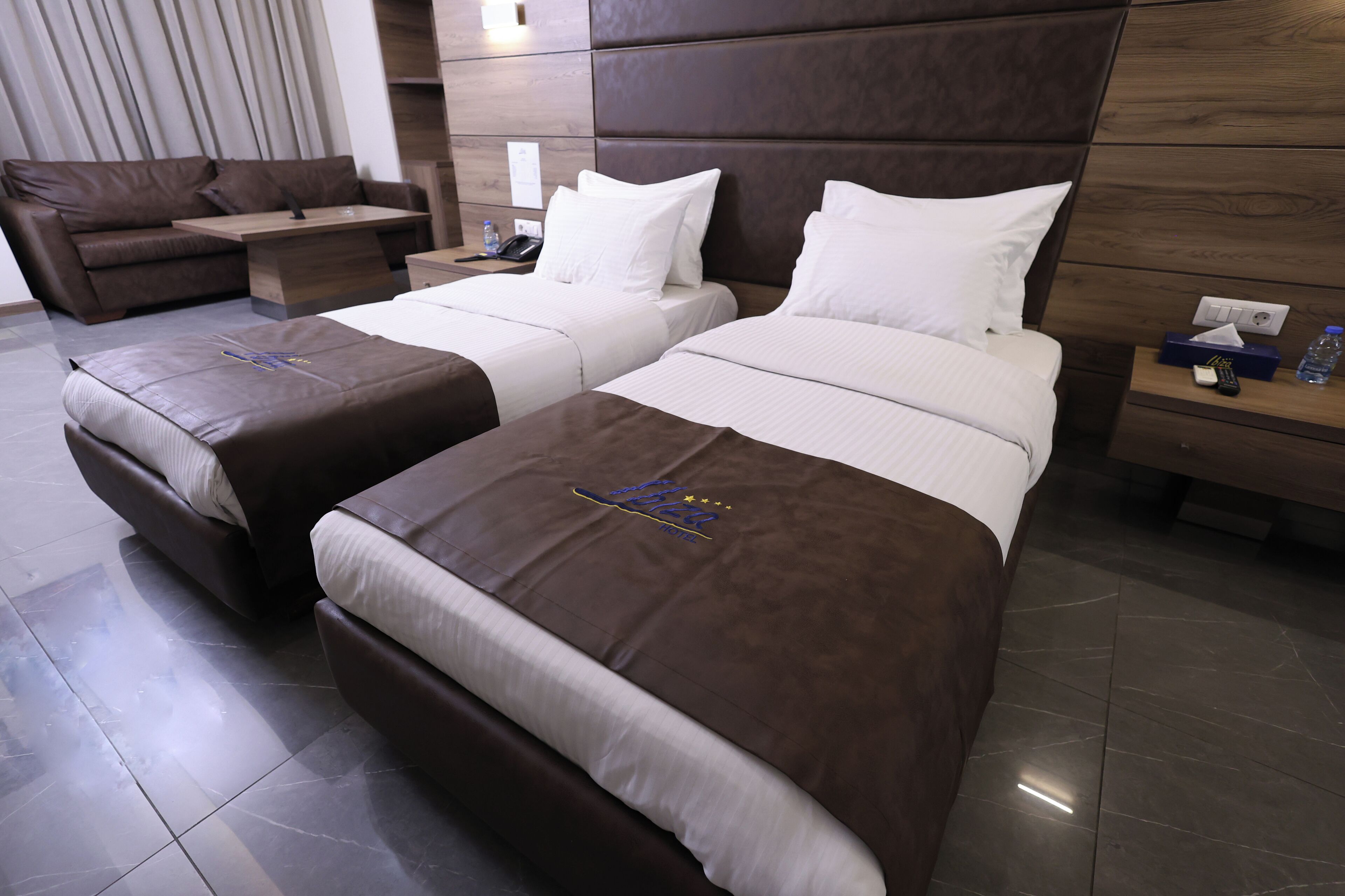 Een hotelkamer met twee bedden, een bank, een bureau en een nachtkastje met een telefoon en een afstandsbediening.