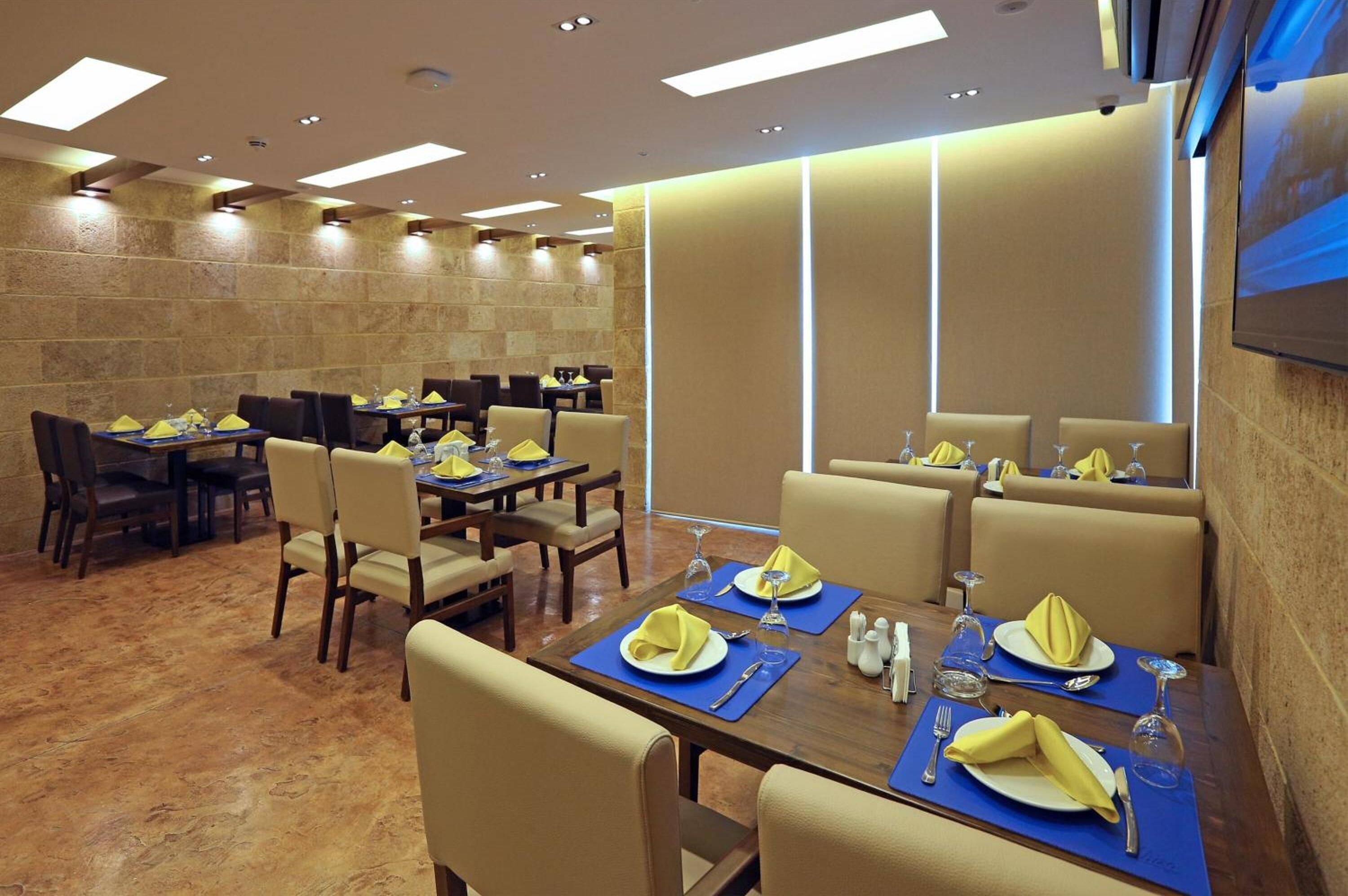 A restaurant with multiple tables set for dining, featuring yellow napkins and wine glasses.