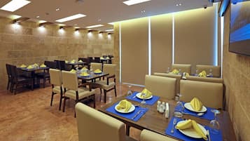A restaurant with multiple tables set for dining, featuring yellow napkins and wine glasses.
