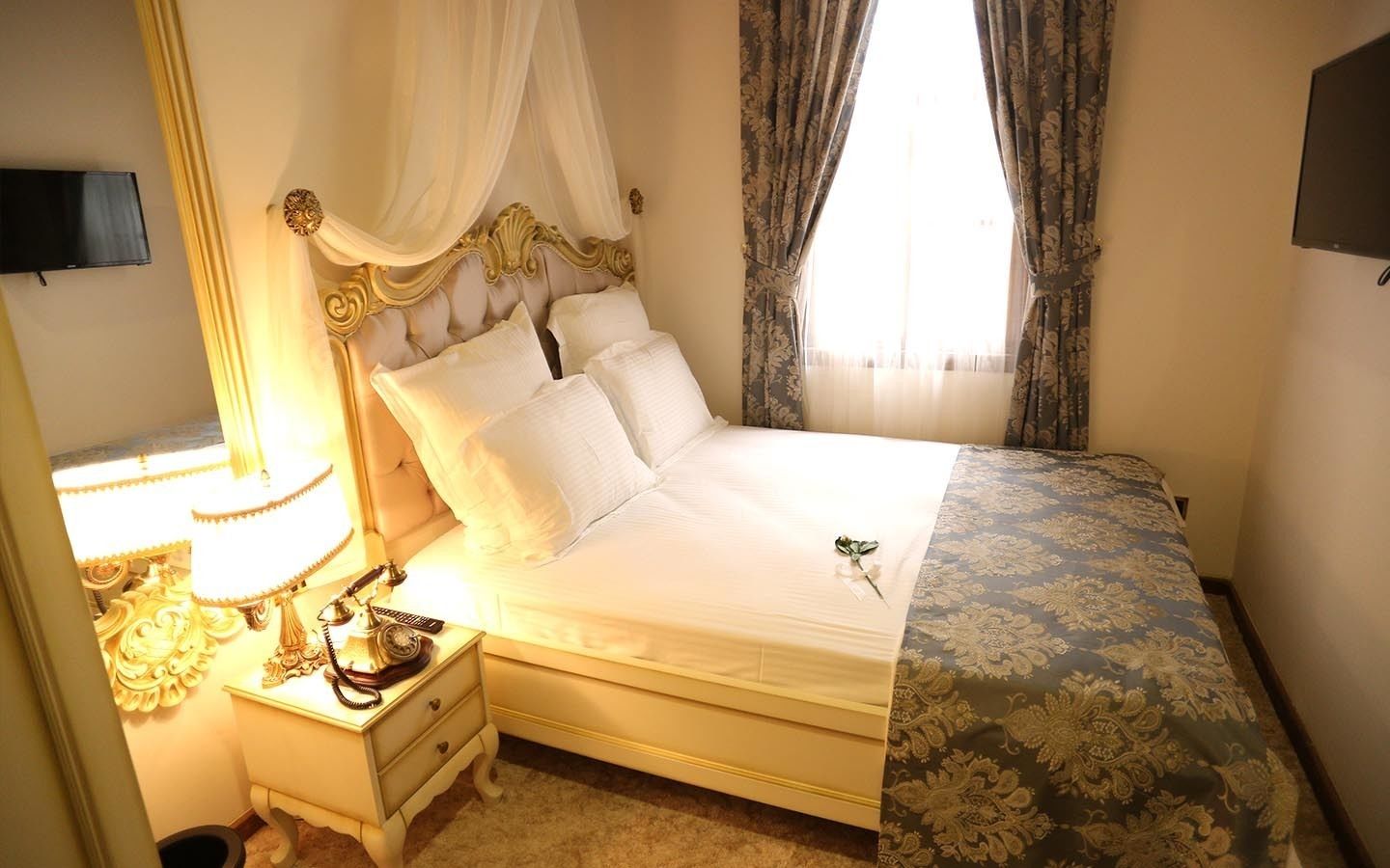 A neatly made bed with a canopy, a bedside table with a lamp, and a television on the wall.