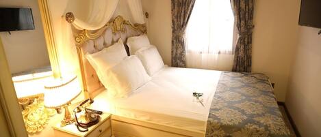 A neatly made bed with a canopy, a bedside table with a lamp, and a television on the wall.