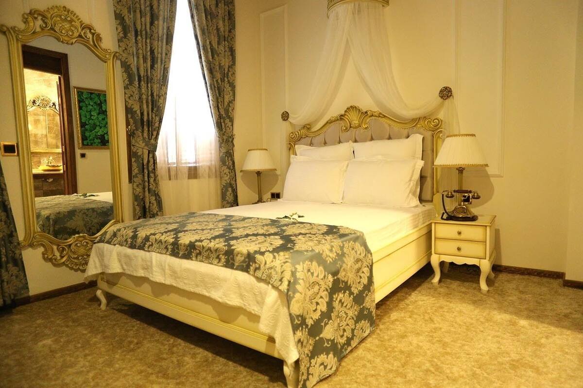 A classic four-poster bed with a canopy, a full-length mirror, and two bedside tables with lamps.