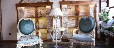 Una habitación con dos sillas ornamentales, una mesita con una lámpara y una pared decorativa con un diseño de ladrillo rústico y un florero.